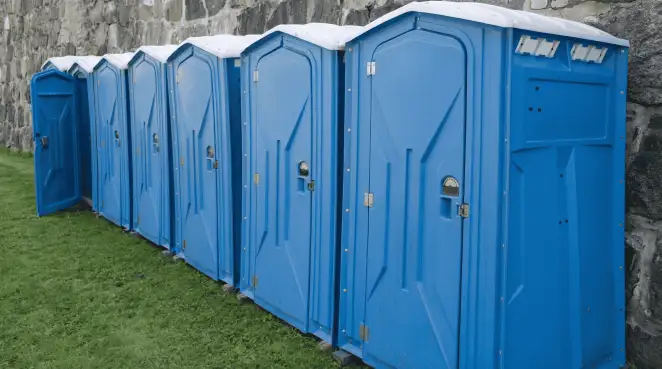 Row of blue portable toilets lined up on grass against a stone wall for event sanitation in El Paso, TX