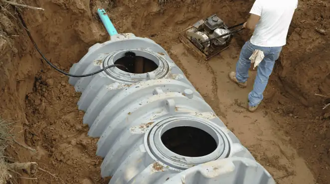 Septic tank installation showing a technician compacting soil around a new poly septic tank in an excavation pit in El Paso, TX
